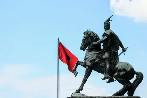 تمثال لرجل على حصان مع العلم الألباني في الخلفية